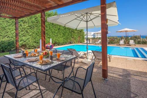 a table with food and an umbrella next to a pool at Villa Krini Eleni in vlicha