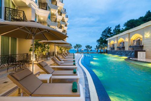 a hotel pool with lounge chairs and umbrellas at LK Emerald Beach - SHA Extra Plus in Pattaya North
