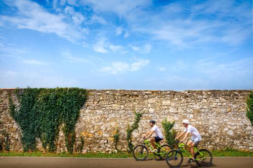 two people riding bikes in front of a stone wall at Aminess Planet Camping Holiday Homes Maravea in Novigrad Istria