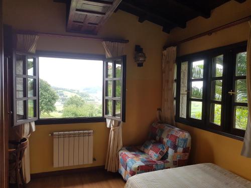 a bedroom with a bed and a chair and windows at Hotel Rural La Curva Ribadesella in Ribadesella