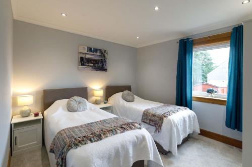 two beds in a room with blue curtains and a window at Lomond Serviced Apartments- Inglewood in Alloa