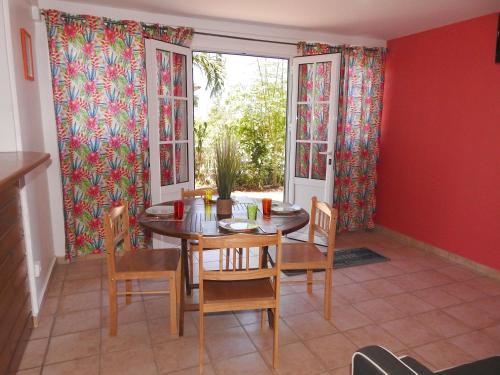 uma sala de jantar com mesa, cadeiras e janelas em GÎTE MORINGA em Bouillante