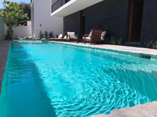 a blue swimming pool with two chairs and a house at Casa Malva in Sayulita