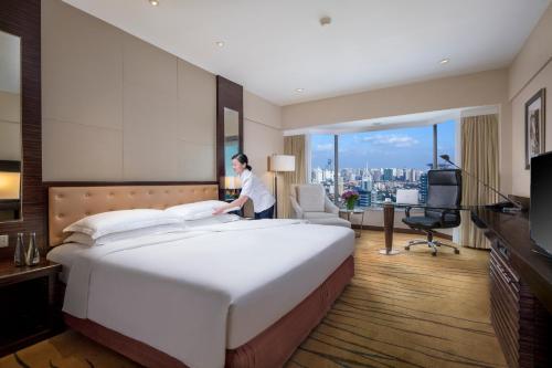 a woman standing next to a large bed in a hotel room at The Kunlun Jing An in Shanghai