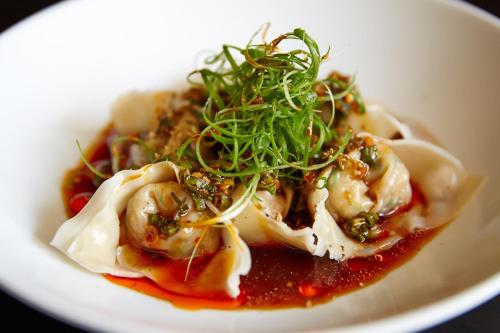 a plate of dumplings with sauce and greens on it at Macleay Hotel in Sydney