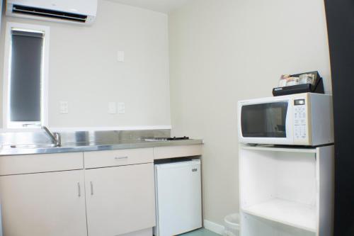 a white kitchen with a microwave and a sink at Rayland Motel in Auckland