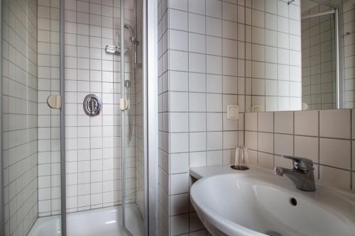 a white tiled bathroom with a sink and a shower at Hotel Goldene Gans in Mannheim