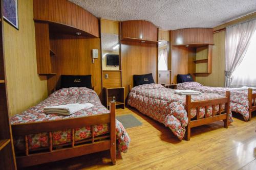 a hotel room with three beds and a television at Hostal Parediso in Punta Arenas