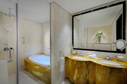 Crowne Plaza - Dubai Jumeirah, an IHG Hotel في دبي: حمام به مغسلتين ومرآة وحوض استحمام