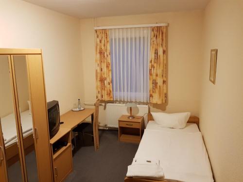 Cette chambre comprend deux lits, un bureau et une fenêtre. dans l'établissement Hotel Merkur Garni, à Sarstedt