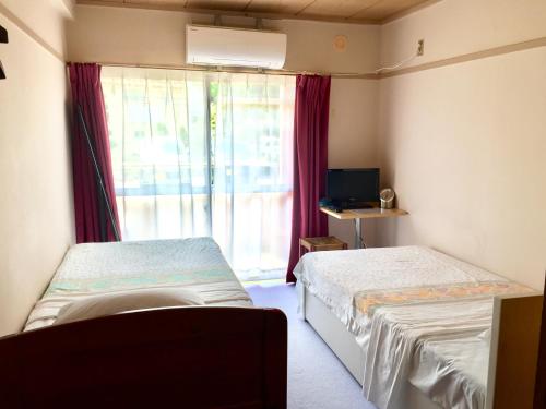 een kleine kamer met 2 bedden en een raam bij Backpackers Dorms Miwa Apartment in Nagano