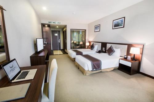 a hotel room with two beds and a desk with a laptop at Muong Thanh Grand Hoang Mai - Nghe An in Hoang Mai