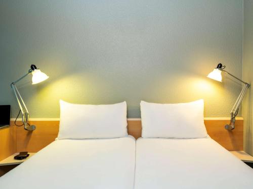 a bed with two pillows and two lights above it at ibis Paris La Villette Cité des Sciences 19ème in Paris
