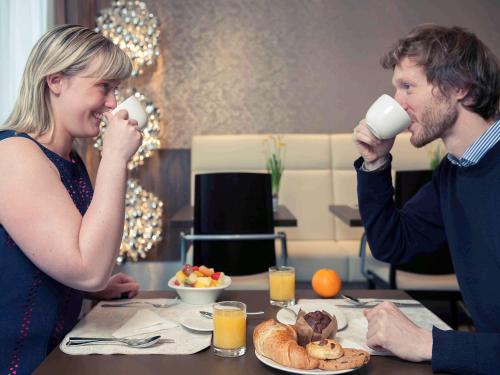 a man and woman drinking cups of coffee at a table at Mercure Hotel Brussels Centre Midi in Brussels