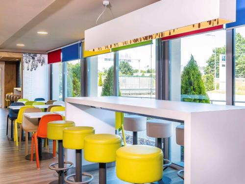 a bar with yellow stools in a room with windows at Ibis Budget Limoges Nord in Limoges