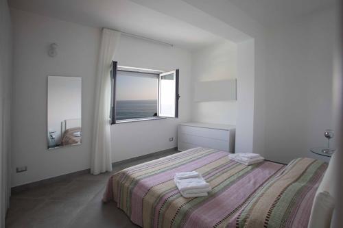 a white bedroom with a bed and a window at Cala Del Faro Beach Villas in Cittadella del Capo