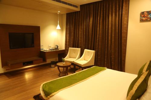 a hotel room with a bed and two chairs and a television at Maple Grand in Agra