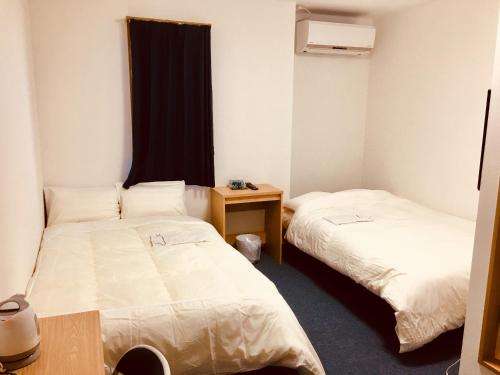 a room with two beds and a table and a window at Hotel Tetora Hachinohe in Hachinohe