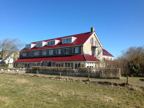 una casa grande con techo rojo en un campo en Hotel Bos en Duinzicht en Nes