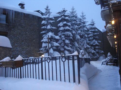 a snow covered christmas tree in front of a fence at Hotel Soldeu Maistre in Soldeu