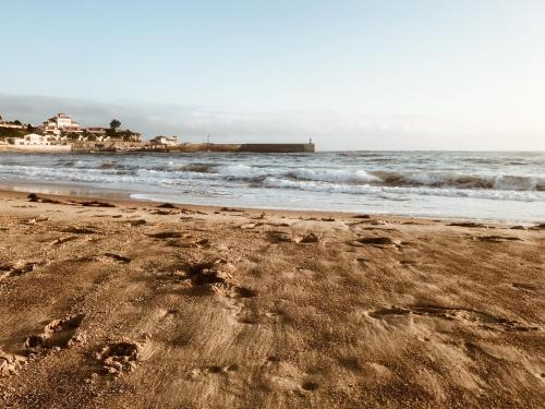 a beach with footprints in the sand and the ocean at Casa de Las Flores - Apartamento con jardín privado frente a la Playa de Comillas in Comillas
