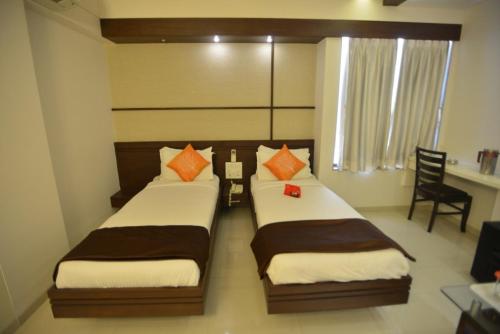 two beds in a small room with a desk and a chair at Hotel Marigold in Vadodara