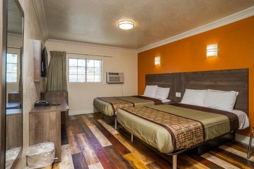 two beds in a hotel room with orange walls at Economy Inn Hollywood in Los Angeles