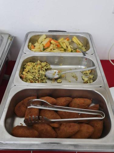 two trays of food with tongs and vegetables in them at Nagar Valley Hotel Ltd. in Dhaka