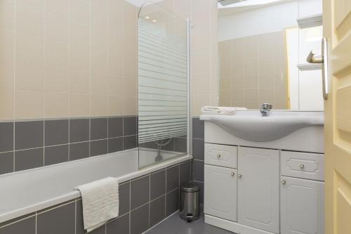 une salle de bain avec un lavabo, une baignoire et un miroir dans l'établissement Résidence Odalys Les Hameaux de Capra Scorsa, à Belgodère
