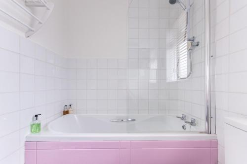 a pink bath tub in a white tiled bathroom at The Mariners Guest House in Poole