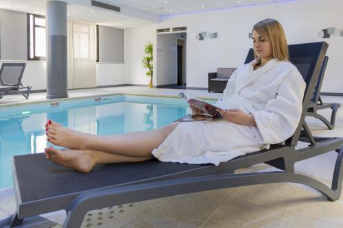 a woman sitting in a chair next to a swimming pool at Hotel Mercure Blois Centre in Blois