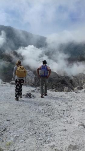 two people with backpacks walking on top of a mountain at De Salak Homestay in Bogor