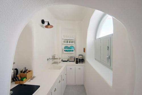 a white kitchen with an arched window and white cabinets at Cave Suite Oia in Oia
