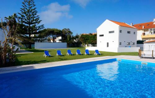 a swimming pool with blue chairs and a house at Silver Seahorse Garden Retreat in Peniche