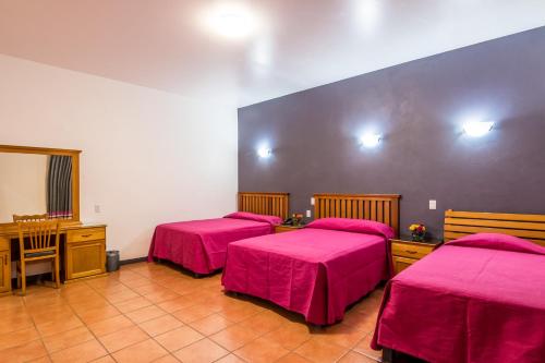 a room with three beds with pink sheets and a desk at Hotel del Marquesado in Oaxaca City