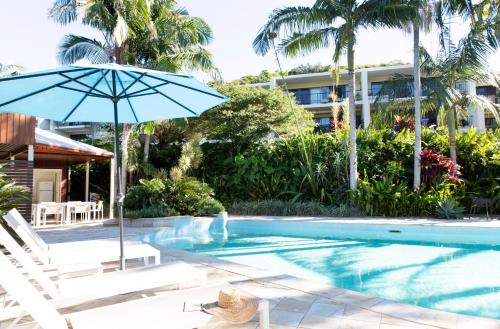 a swimming pool with a blue umbrella and a chair at The Oasis Apartments and Treetop Houses in Byron Bay