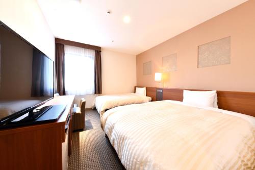 una camera d'albergo con due letti e una televisione di Vessel Inn Yachiyo Katsudai Ekimae a Yachiyo