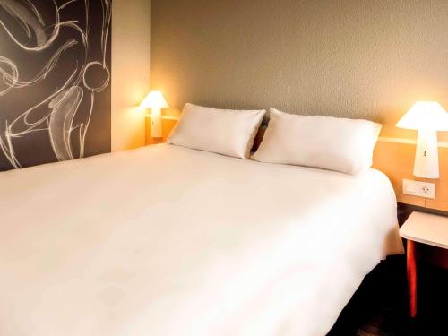 a large white bed in a room with two lamps at ibis Bayonne Centre in Bayonne