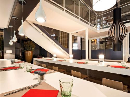 a restaurant with white tables and chairs and a staircase at ibis Site du Futuroscope in Chasseneuil-du-Poitou