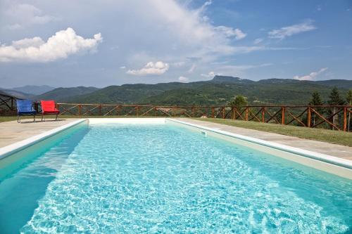 a swimming pool with two chairs and mountains in the background at Antico Casale di Ferdinandi in Bibbiena