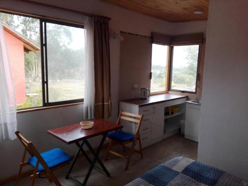 una pequeña cocina con mesa, sillas y ventanas en Cabañita Totoverde, en El Totoral