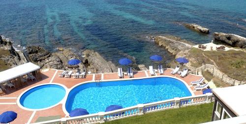 a pool with chairs and umbrellas next to the ocean at Villa Las Tronas Hotel & SPA in Alghero