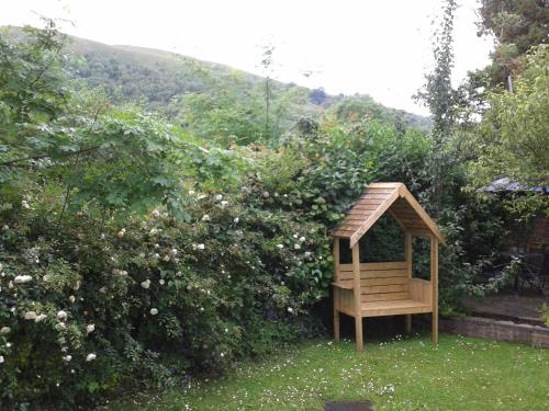 a wooden gazebo in the grass next to a bush at Railway Cottage in Cardiff