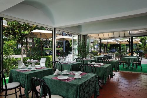 un restaurante con mesas verdes, sillas y ventanas en Hotel Suisse, en Milano Marittima