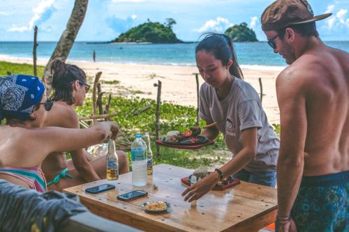 a group of people sitting at a picnic table on the beach at Mad Monkey Hostel Nacpan Beach in El Nido