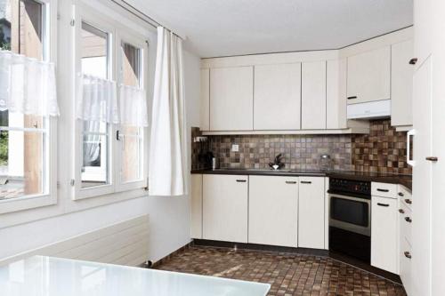 cocina con armarios blancos, fregadero y ventana en Ferienwohnung Bahnhöfli, en Lauterbrunnen