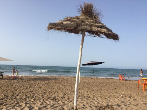 a straw umbrella on a beach near the ocean at Perle Orientale Saidia Appart Rénové vue sur jardin et sur mer in Saidia 