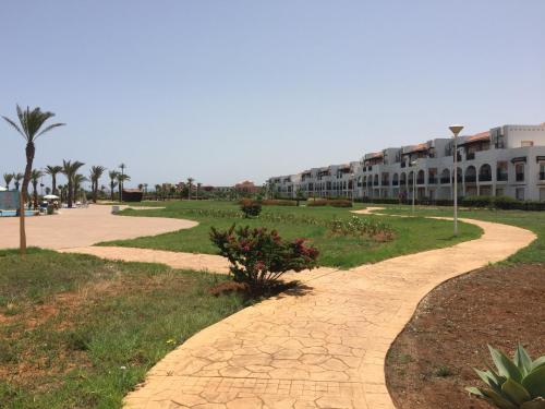 a walkway in front of a building with palm trees at Perle Orientale Saidia Appart Rénové vue sur jardin et sur mer in Saidia 