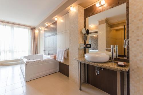 uma casa de banho com uma banheira e um lavatório e uma banheira em Hunguest Hotel Apollo em Hajdúszoboszló
