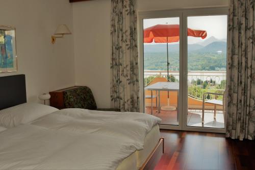 a bedroom with a bed and a balcony with an umbrella at Aparthotel Claudia in Velden am Wörthersee